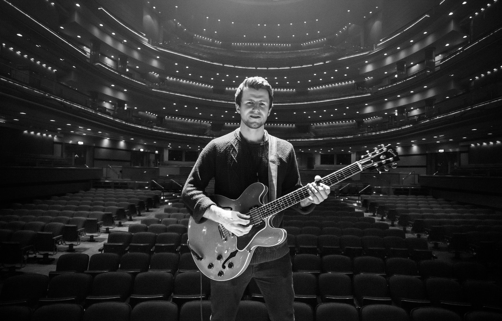 David Niskin performing guitar in a large concert hall.